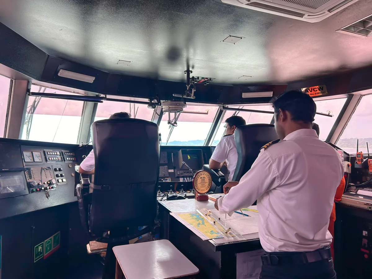 On the bridge — the captain and officers plotting the crossing Makruzz bridge crew navigating with charts and instruments, an operational-excellence award on the console